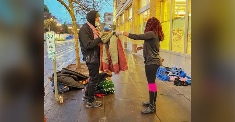 Sara Edmond offers a warm coat to a homeless man outside Blanchet House.