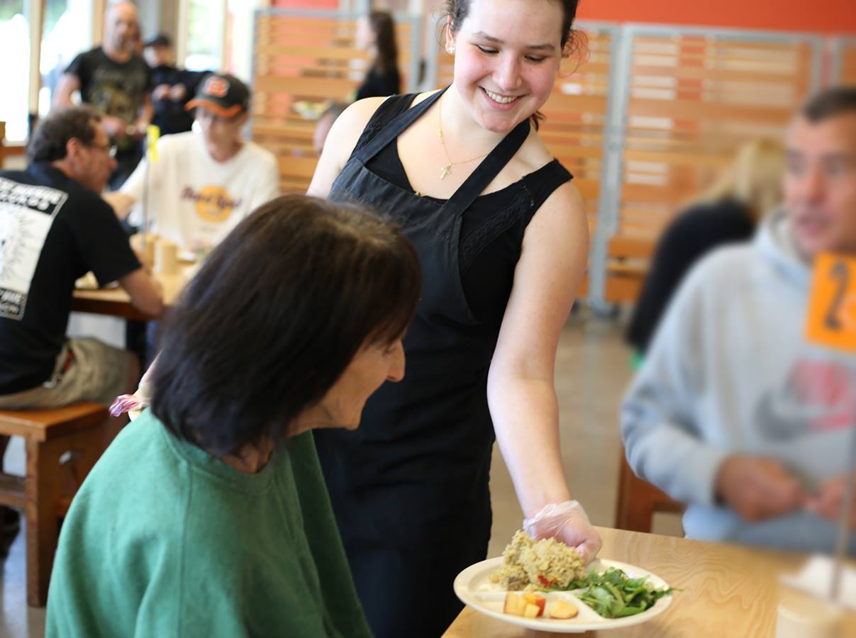 Volunteer serves a meal to a guest in Blanchet House of Hospitality's cafe.
