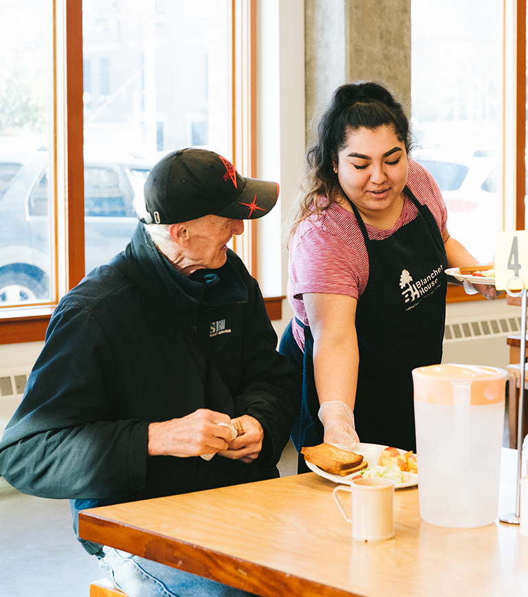 Volunteer serves a man a meal at Blanchet House