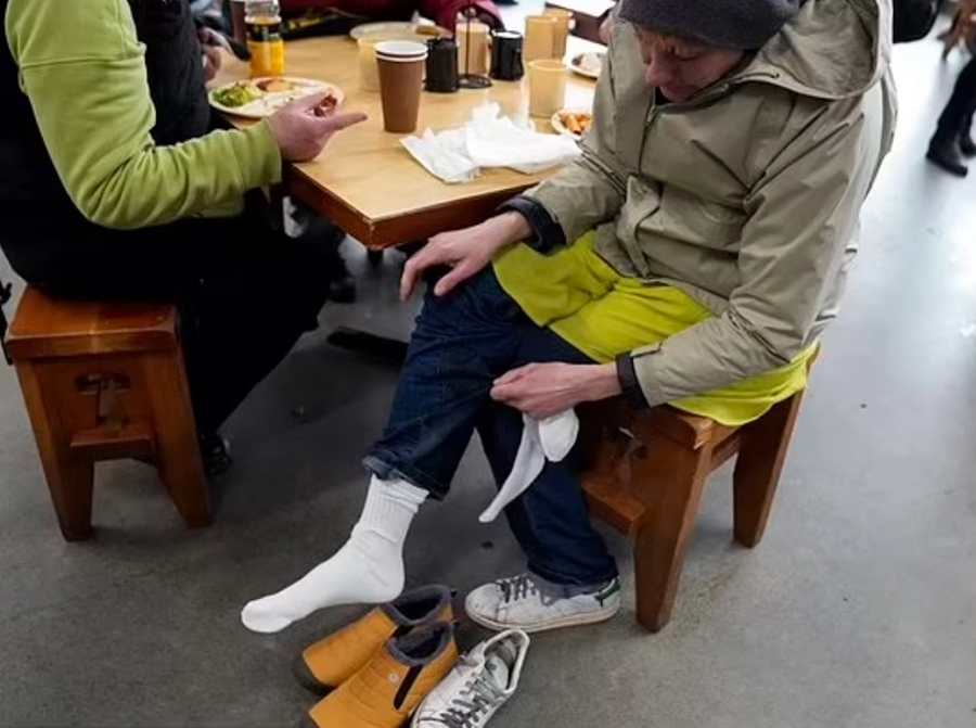 A woman puts on dry socks and shoes in the cafe at Blanchet House. The 2023 Point in Time count of homelessness show's an increase in women experiencing homelessness in Portland, Oregon. 